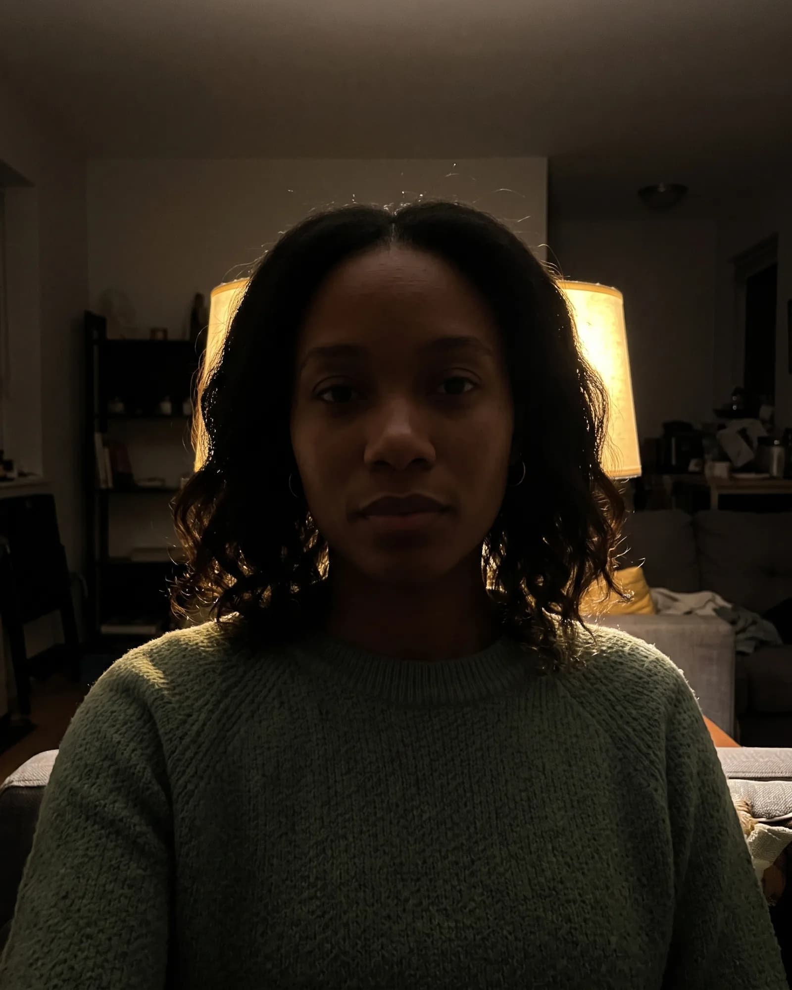 The same woman lit from behind by a lamp in a dark room.