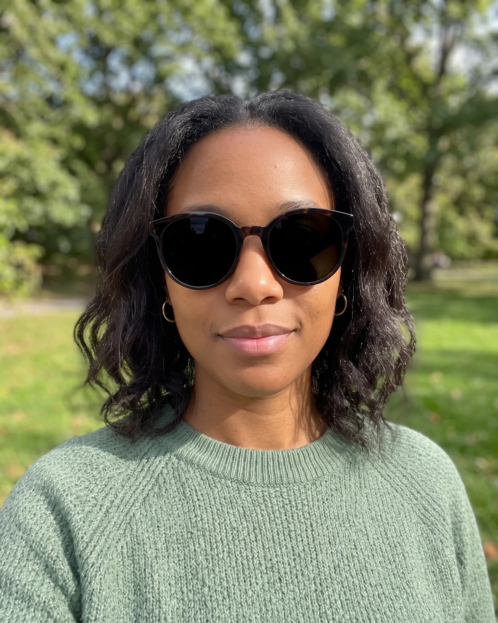 The same woman outdoors in large dark sunglasses that hide her eyes.